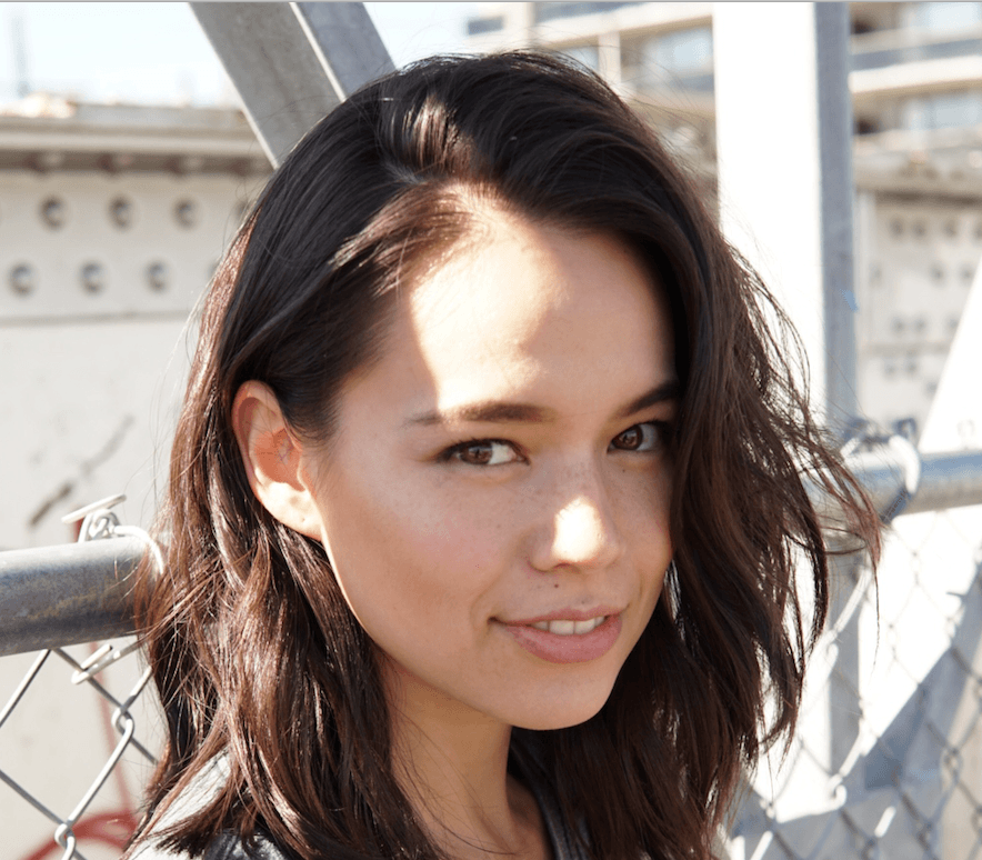 Close up of a woman, Genevieve Kang, standing on a bridge and smiling.