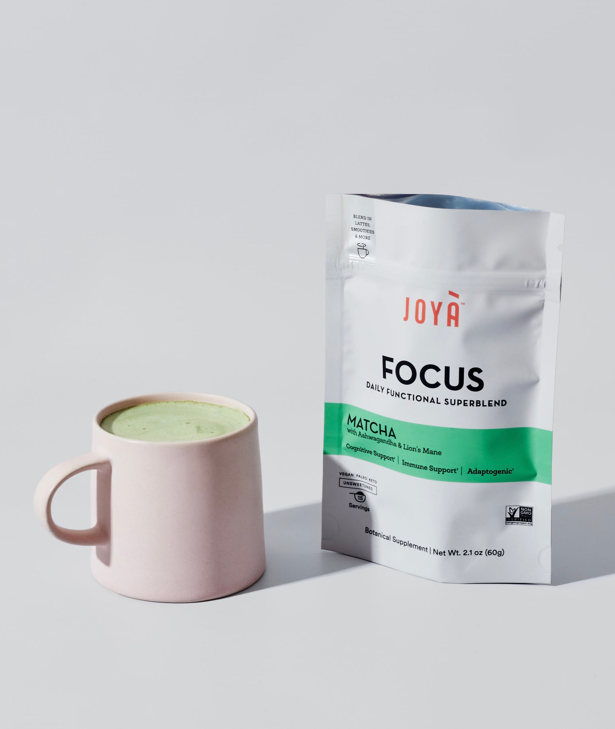 Matcha latte in a pink mug next to a pouch of JOYÀ Focus Matcha Superblend