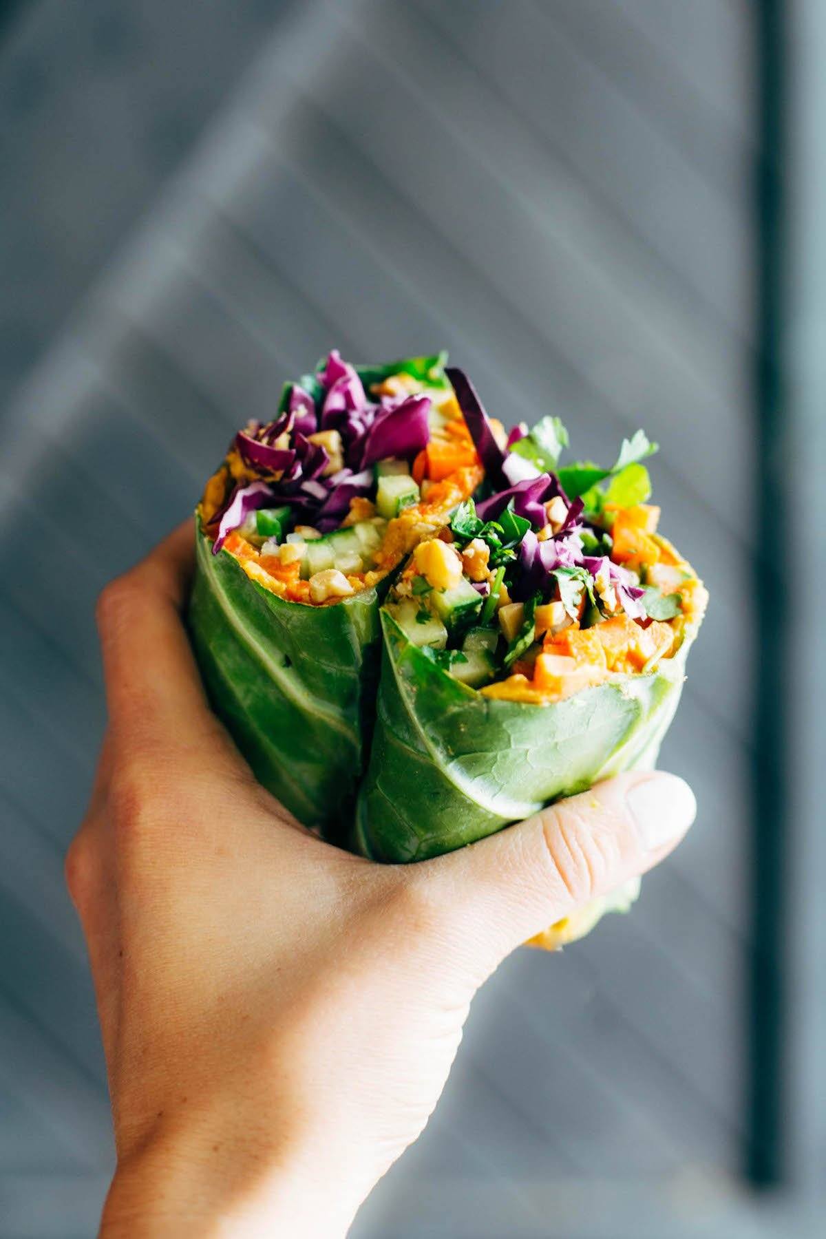 A hand holds a green vegetarian wrap made out of collard green leaves. 