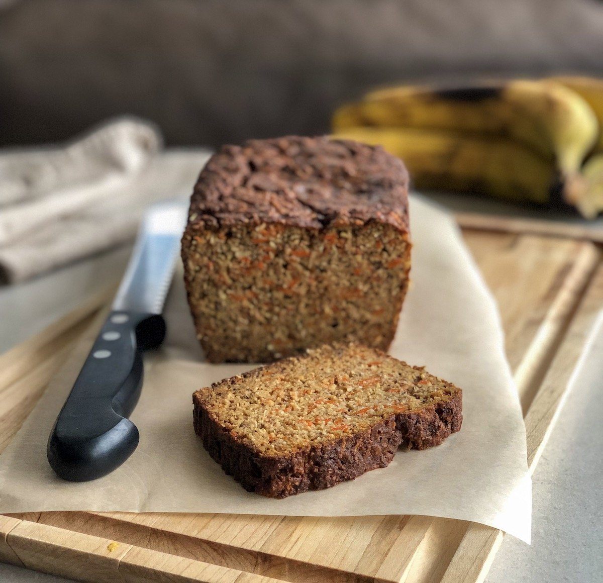 morning glory loaf on bread board next to knife with bananas in the background