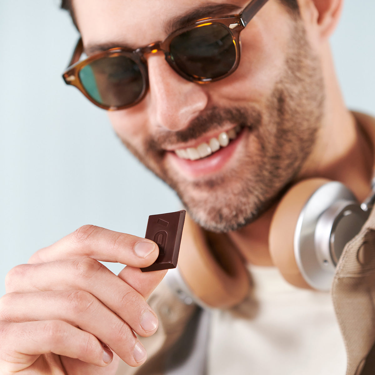 Young man wearing sunglasses and headphones ready for travel enjoying a piece of Defend Functional Chocolate