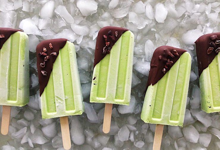 Vegan and dairy-free matcha mint popsicles coated in a chocolate magic shell on a bed of ice.