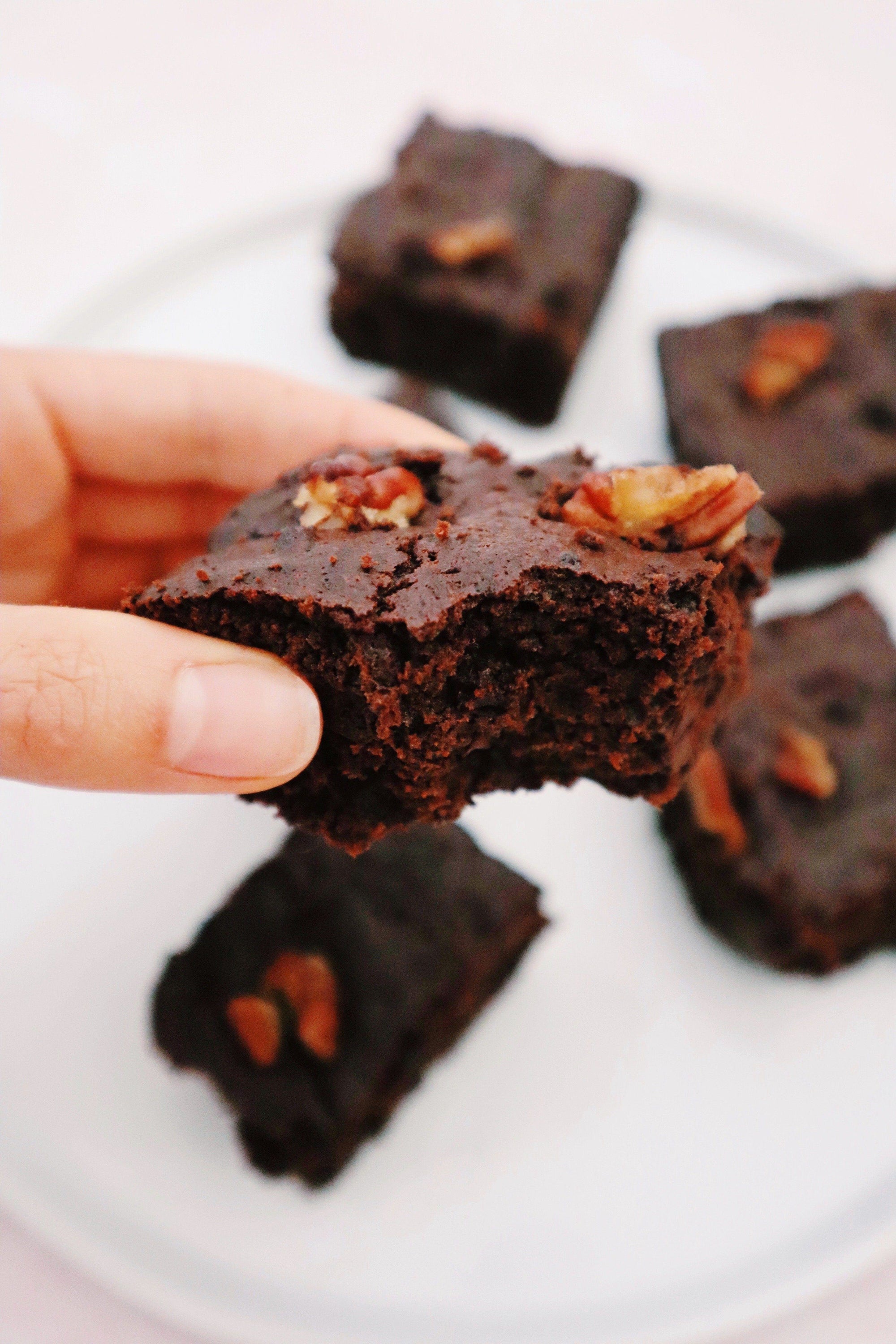 Hand holding paleo brownies featuring recipe with JOYÀ Bliss Elixir
