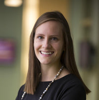 Smiling young woman, Beth Bierema, in office clothes and a long beaded necklace.