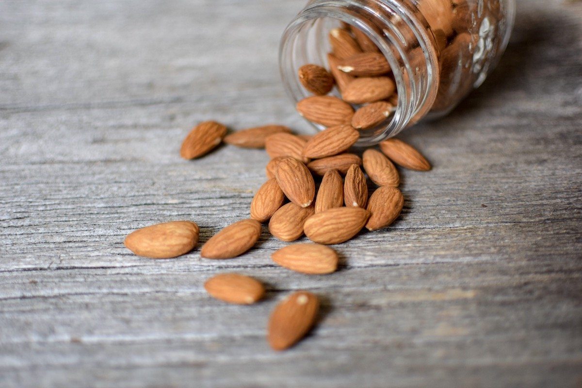 A small mason jar of activated almonds spills out across a wooden table. 