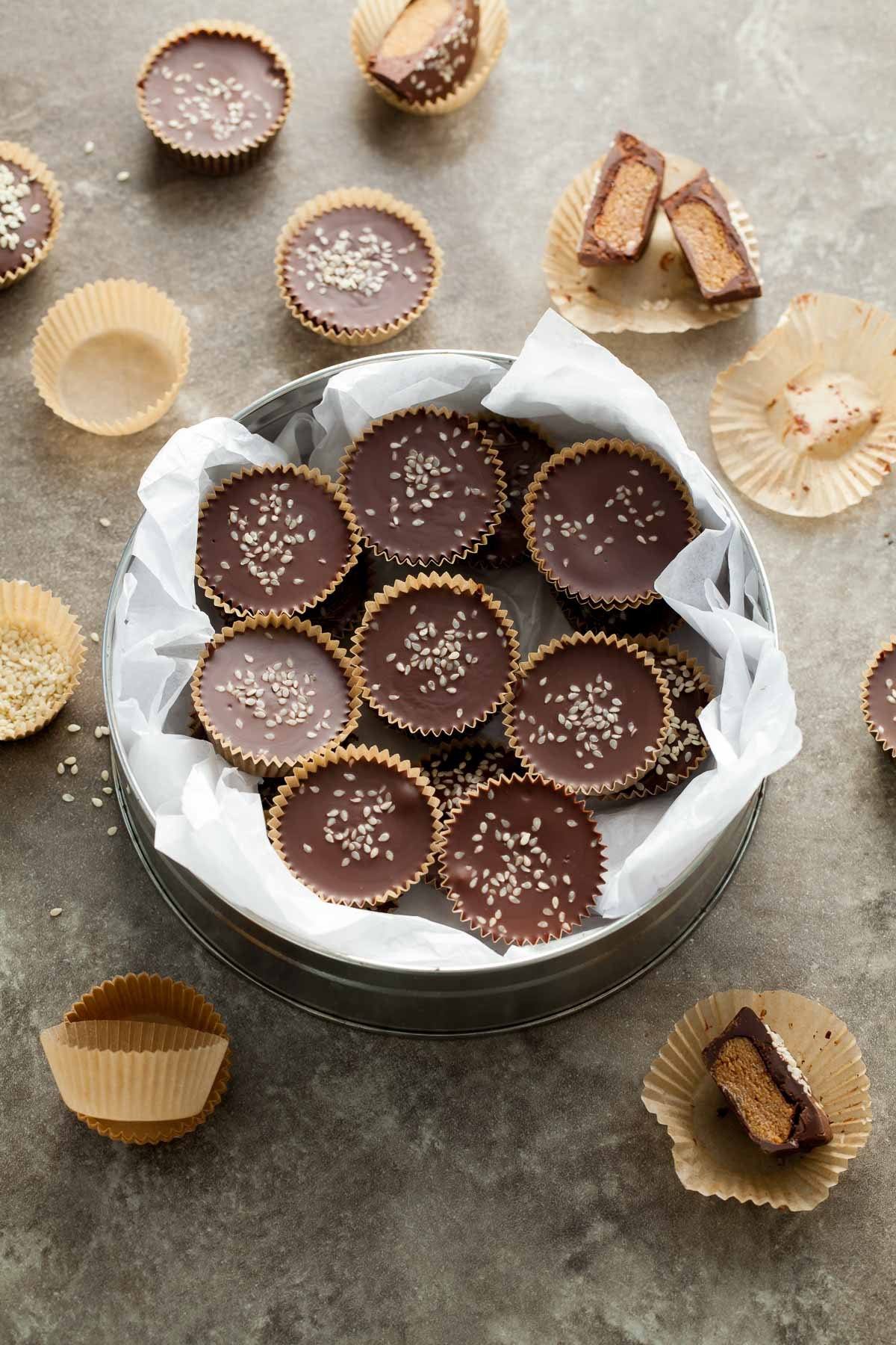 A bowl of vegan and paleo dark chocolate tahini cups with sesame sweets sprinkled on top. 