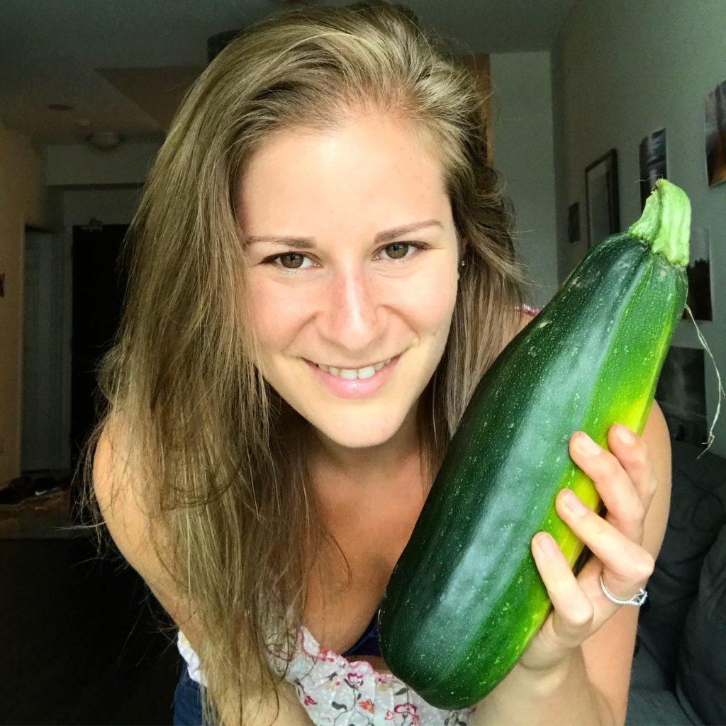 Young woman smiles holding a zucchini.