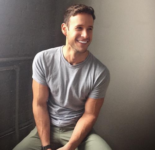 Young fit man, Kyle Buchanan, sitting on a stool and smiling.
