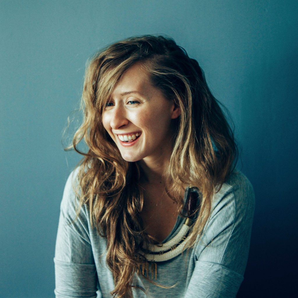 Young woman, Laura Wright, smiles and laughs in front of a blue wall.