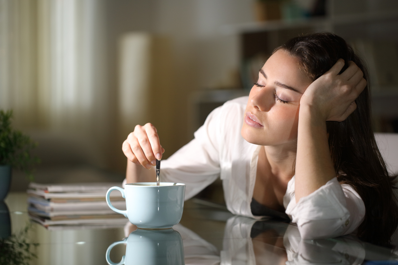 Young woman falling asleep while stirring coffee
