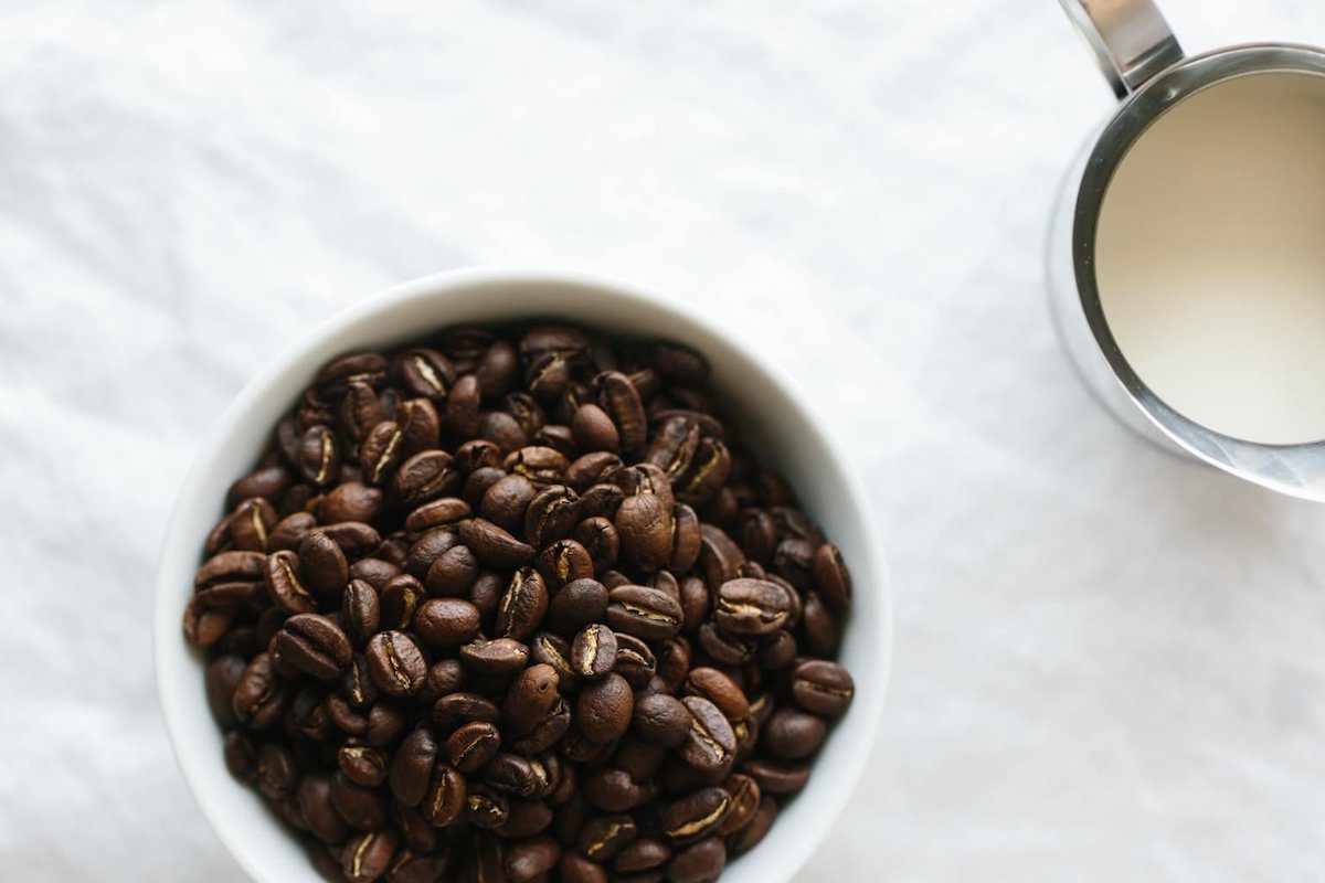 espresso beans in a bowl with a cup of milk