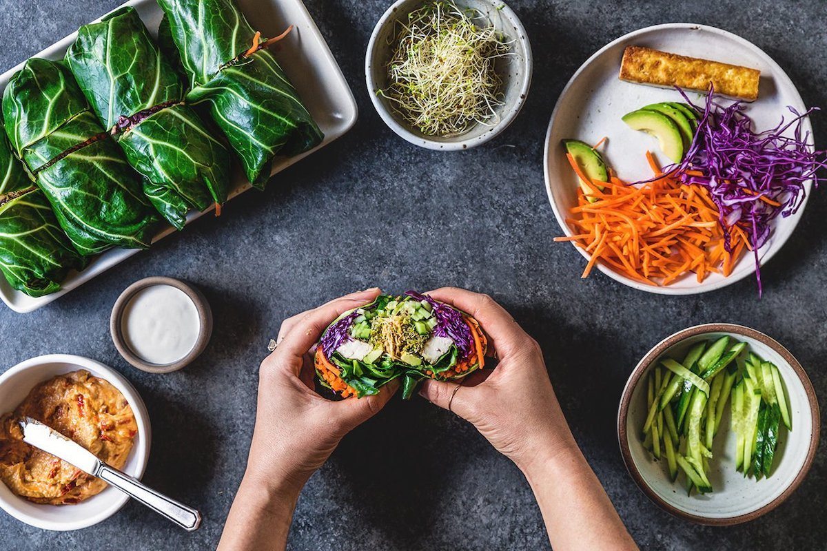 extra large lettuce wraps being held by hands with ingredients in bowls shredded carrot sprouts
