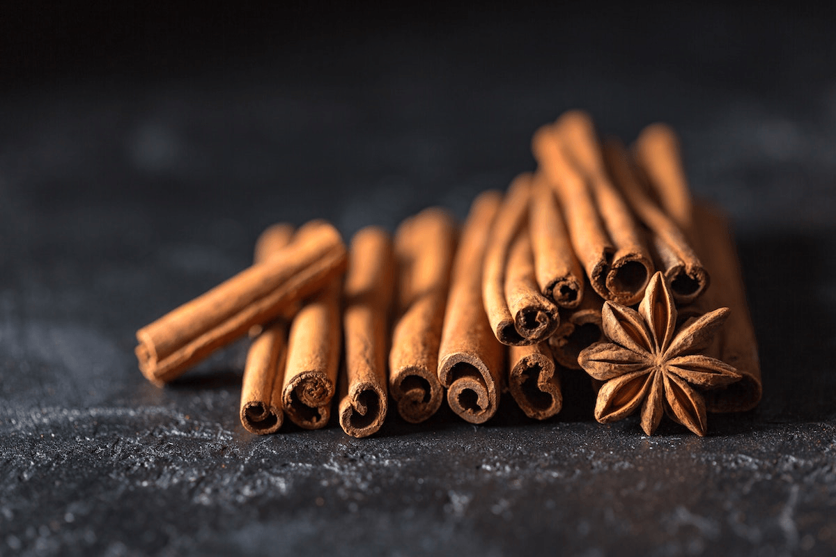 A stack of warm brown cinnamon sticks against a black backdrop with a dried star anise pod. 