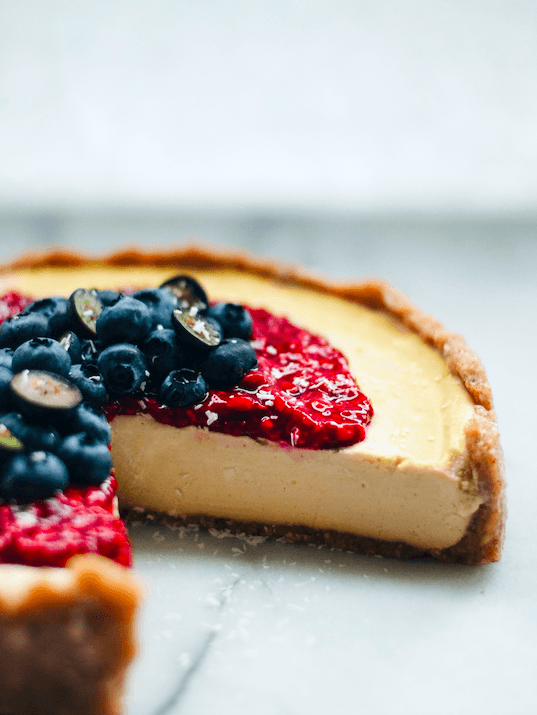 close up of lemon tart topped with blueberries with a big slice missing