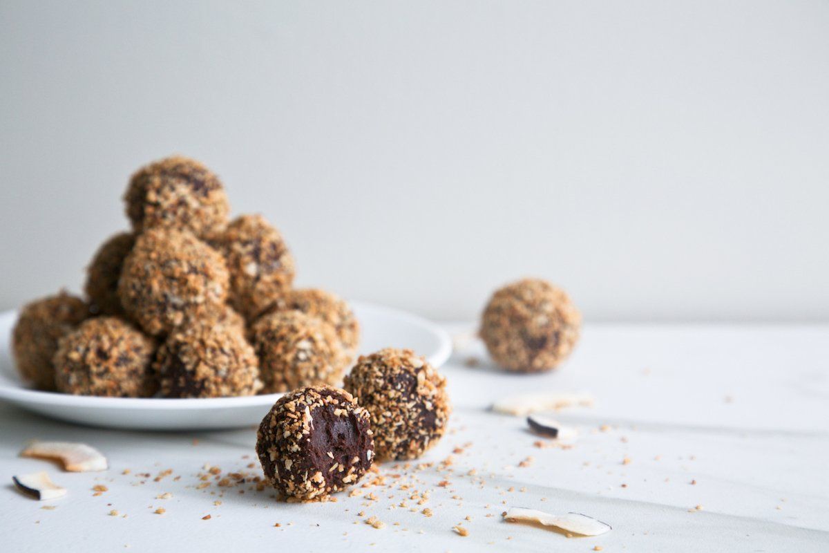 vegan chocolate truffles stacked on a white plate dusted with toasted coconut