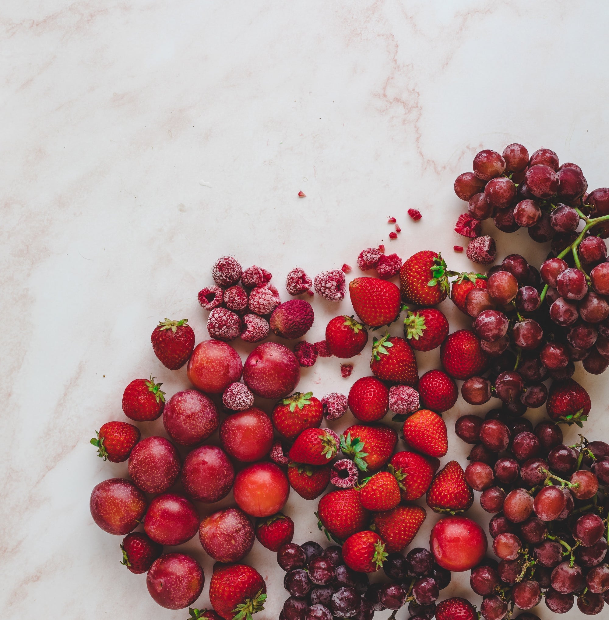 Overhead image of red fruit like strawberries, plums, raspberries and grapes