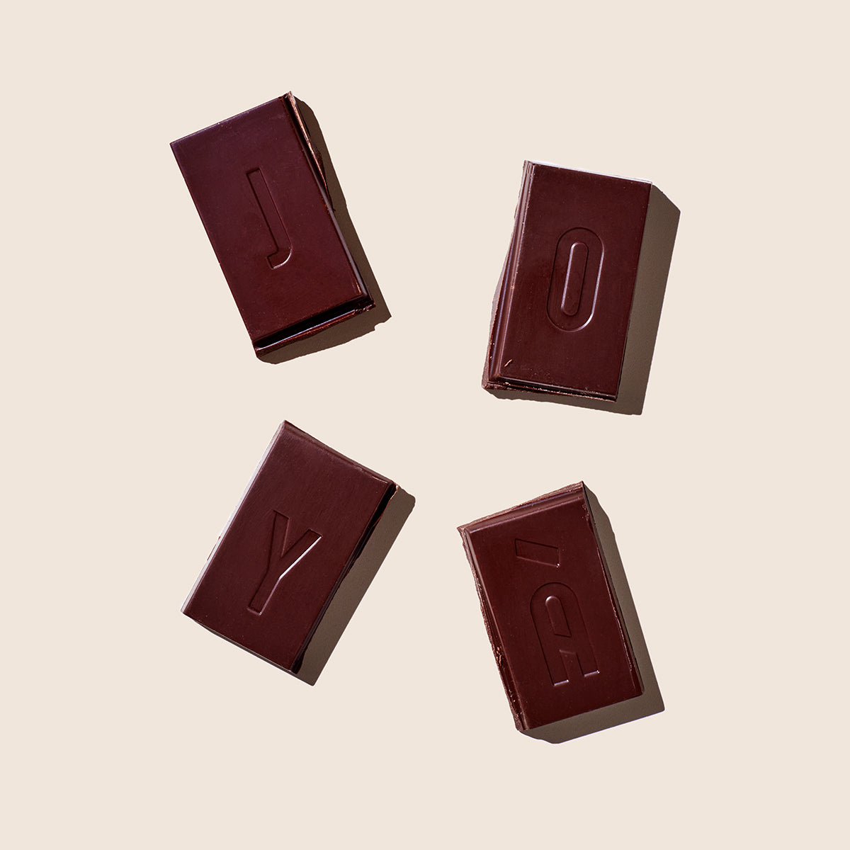 JOYÀ Functional Chocolate bar broken into four squares lying on a beige tabletop