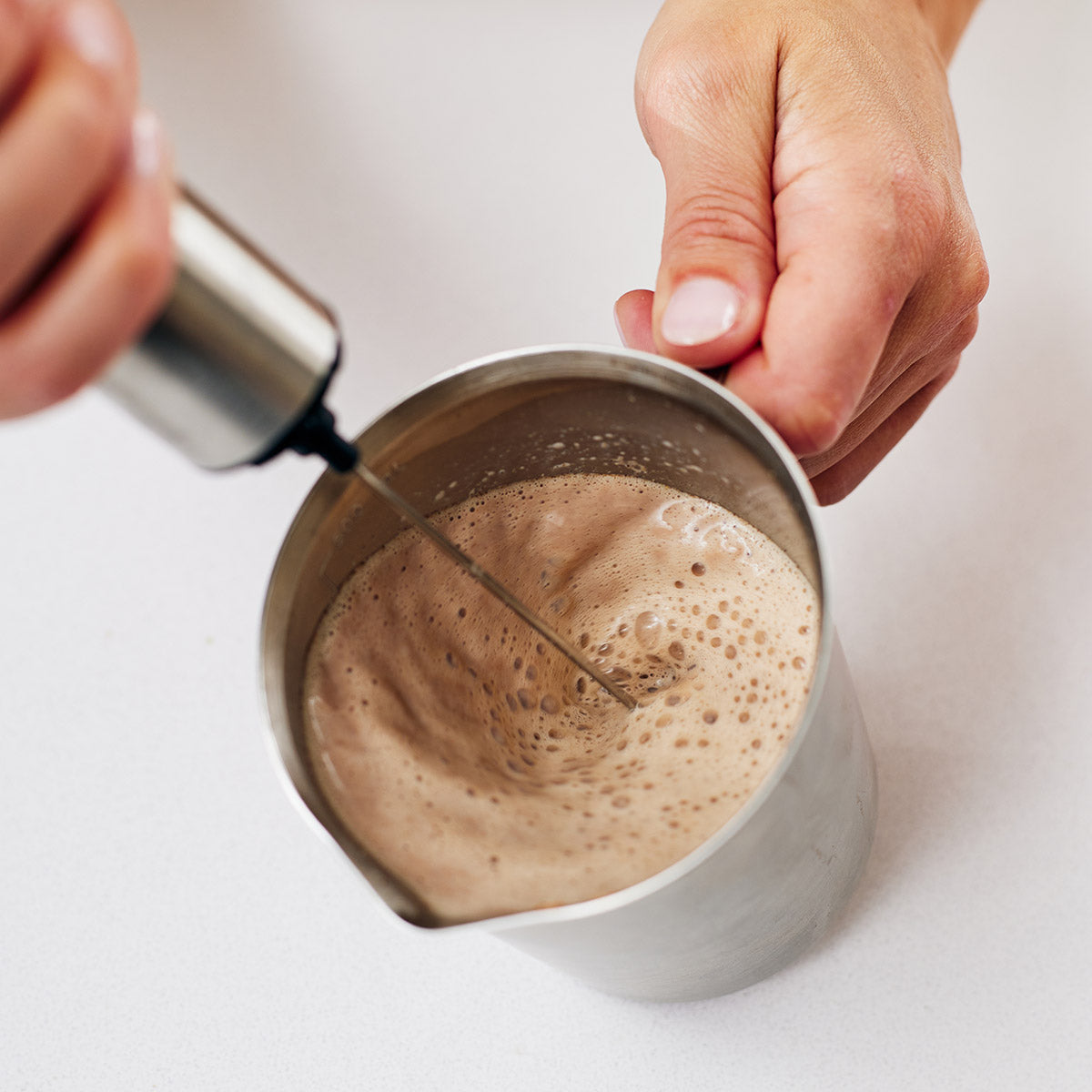 Woman mixing a Calm cacao latte with rechargeable frother in a silver mixing mug