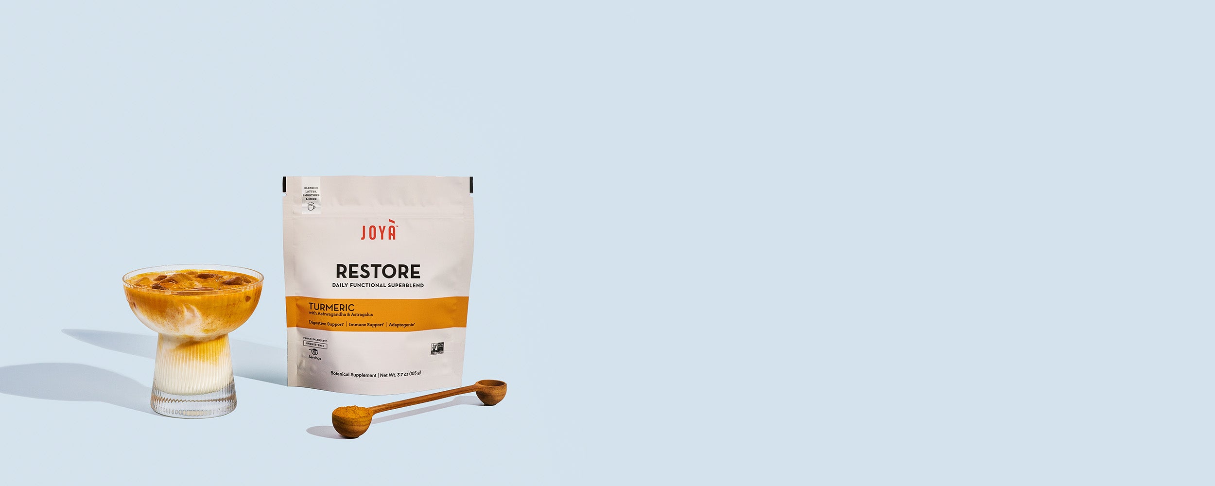 Restore Superblend 15-serving pouch sitting beside a wooden spoon and iced Restore turmeric latte in a clear glass on a blue background